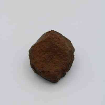 Closeup of basaltic glass core: The image shows a rough, angular piece of basaltic glass with a dark, earthy brown color, set against a plain white background.