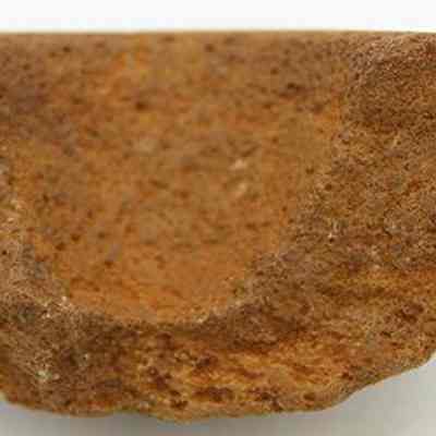 Profile of cup or mortar fragment: The image depicts a rough, brown, partially curved fragment, possibly from a cup or mortar, showing weathered and uneven textures, against a plain background.