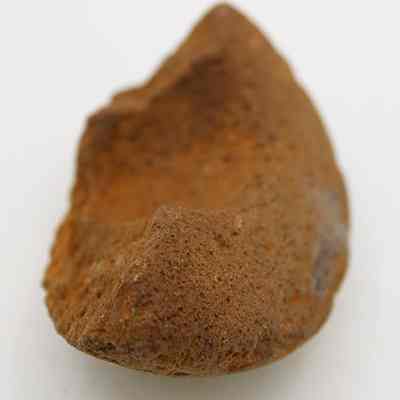 Closeup of cup or mortar fragment: The image shows a rough, brown fragment of an ancient stone cup or mortar, with a textured surface and a jagged, irregular edge.