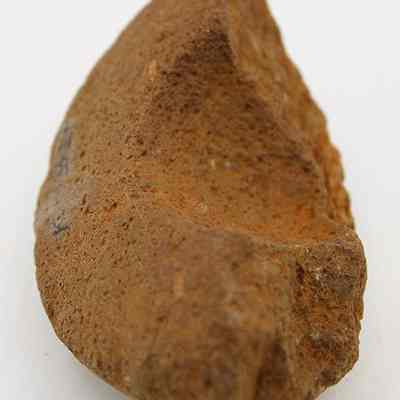 Close up of fragment of a cup or mortar: The image shows a rough, worn fragment with an earthy texture and brownish hue, possibly a piece of an ancient cup or mortar.