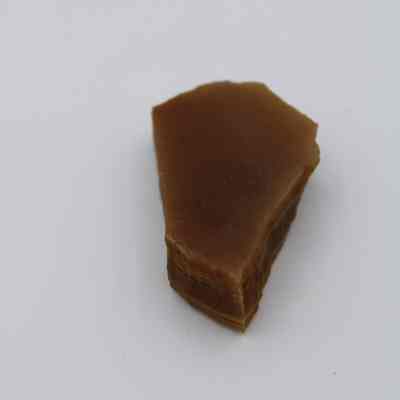Lengthwise view of an agate flake: The image shows a small, angular agate flake with a brownish hue, resting on a plain white surface, highlighting its layered texture.