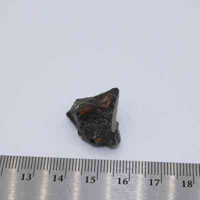 Closeup of small basaltic glass core: A small piece of basaltic glass core is placed on a white surface, accompanied by a ruler measuring its size.