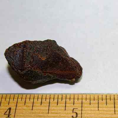 Two pieces of volcanic glass: Two reddish-brown rocks of different sizes are placed on a sheet beside a wooden ruler.