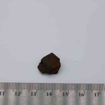 Closeup of basaltic glass core with ruler: A small basaltic glass core rests against a measuring scale on a plain surface, highlighting its compact size.