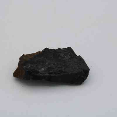 Closeup of basaltic glass flake: The image shows a small, dark basaltic glass flake with rough, uneven edges resting on a light-colored surface.