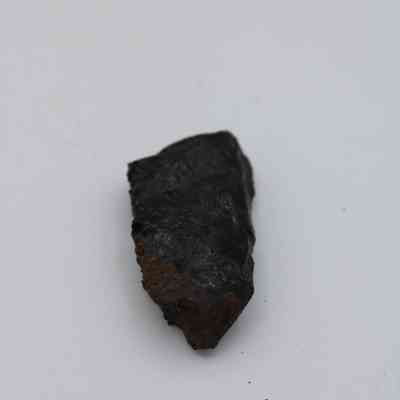 Lengthwise view of basaltic glass flake: The image shows a dark, unevenly shaped basaltic glass flake with a glossy texture, set against a plain white background.