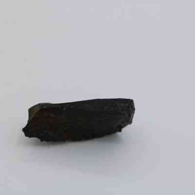 Profile of basatlic glass flake: The image shows a single flake of basaltic glass resting on a smooth, light-colored surface, highlighting its dark, glossy texture.