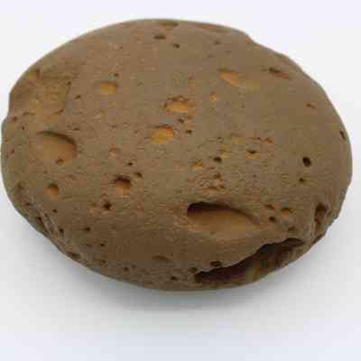 Closeup of worked cobble stone: The image shows a closeup view of a worked cobblestone, highlighting its smooth, weathered surface with distinct, rounded indentations and earthy tones