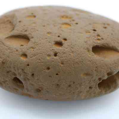 Close up of worked cobblestone: The image depicts a round, brown cobblestone with numerous small holes and a rough, textured surface.