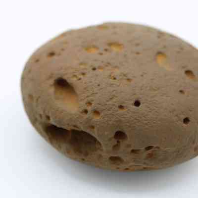 Worked cobble stone: The image shows a worked cobblestone with a smooth, rounded shape and small holes on its brown surface.