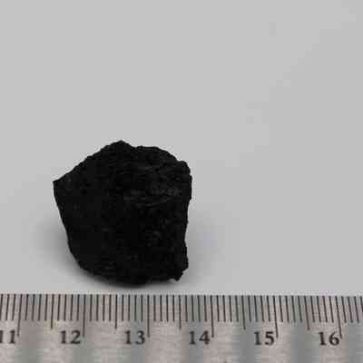 Closeup of basaltic glass flake with ruler: A small piece of basaltic glass flake is placed against a plain background, with a ruler for scale in the foreground.