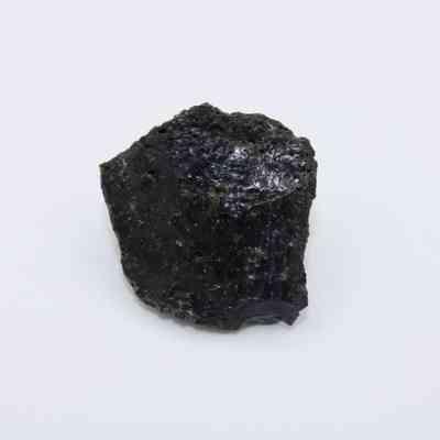 Closeup of basaltic glass flake: The image shows a dark, irregularly shaped piece of basaltic glass flake with a shiny, reflective surface on a white background.