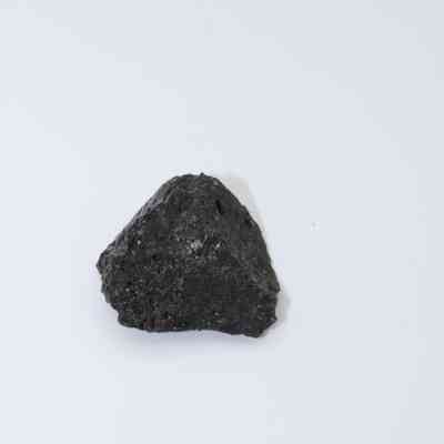 Closeup of basaltic glass flake: A single, dark basaltic glass flake with a rough texture is centrally placed against a smooth, light background.