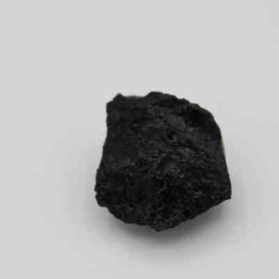 Extreme closeup of basaltic glass flake: A black basaltic glass flake is positioned against a plain white background, showcasing its rough and irregular texture.