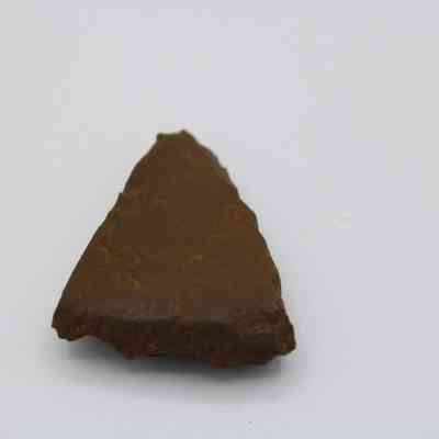 Triangular adze fragment: The image displays an ancient stone tool, resembling an adze blade, crafted from a piece of brown rock with a sharp edge.
