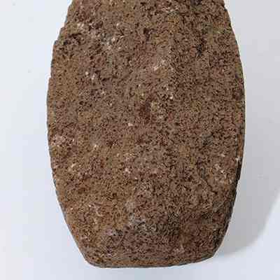 An 'ulu maika fragment with a ruler: The image shows a rough, brown, elongated stone with a textured surface placed on a white background, aligned next to a ruler for scale measurement.