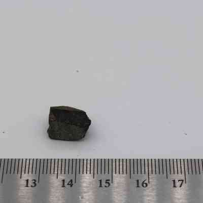Small basaltic glass flake with ruler: A small basaltic glass flake rests on a white surface, positioned alongside a ruler for size reference.