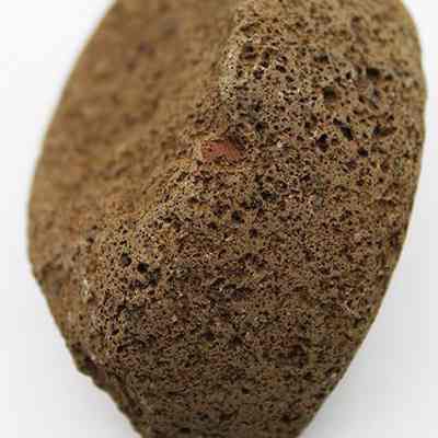 Sideview of an 'ulu maika fragment with a ruler: The image depicts a porous, brown volcanic rock with visible texture, positioned against a plain background, and a ruler beneath indicating its size in centimeters.