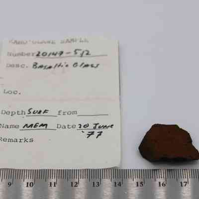 Small basaltic glass flake with artifact slip and ruler: The image displays a basaltic glass flake sample alongside a labeled slip and a ruler for scale.
