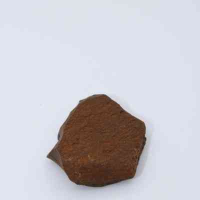 Closeup of basaltic glass flake: The image shows a single, dark basaltic glass flake with a rough, textured surface, lying on a smooth, white background.