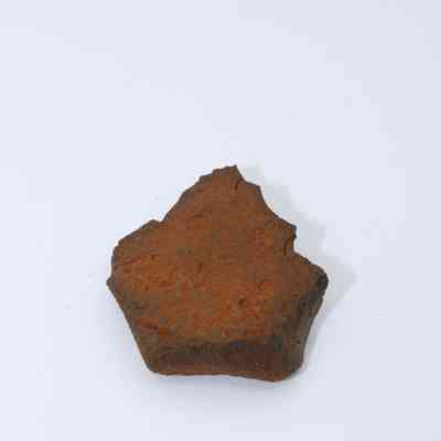 Closeup of basaltic glass flake: A basaltic glass flake lies on a plain surface, exhibiting an uneven texture with a distinctive brown hue.