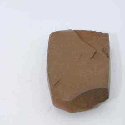 Lengthwise closeup view of polished flake: The image depicts a single polished stone flake, resting on a plain, white background, with visible smooth and slightly irregular surfaces.