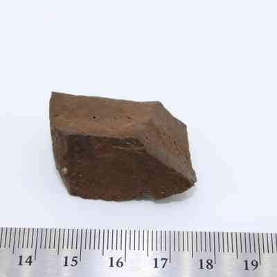 Profile of glass core with ruler: A small, angular brown glass core is placed on a plain white background with a ruler measuring its dimensions precisely.