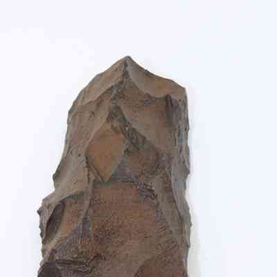 Lengthwise view of adze fragment: The image depicts a weathered, stone adze fragment with sharp edges, showcasing its crafting technique on a plain white background.