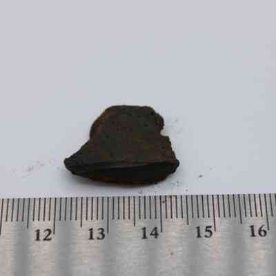 Basaltic glass piece with metal ruler: A small piece of basaltic glass rests on a plain surface, measuring approximately 2.25 millimeters, with a metal ruler for scale underneath.