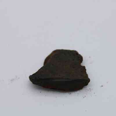Close up of basaltic glass: The image shows a small piece of basaltic glass with a dark, irregular surface, resting on a light background.