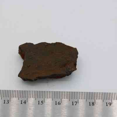Basaltic glass core with ruler: A small, rugged piece of basaltic glass core is displayed next to a metal ruler on a white surface.