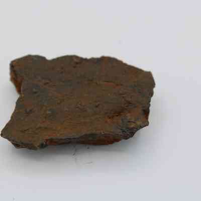 Closeup of a basaltic core: The image shows a rough, dark-brown basaltic core with textured surfaces on a plain, white background.