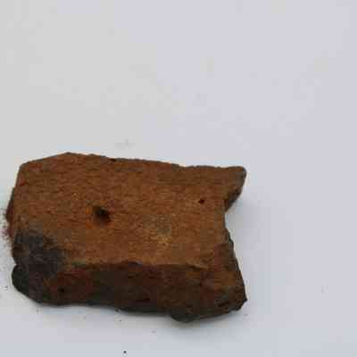Closeup of basaltic glass core: A piece of basaltic glass core lies on a white surface, showing a rough texture and small visible holes.