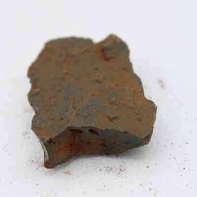 Closeup of basaltic glass core: The image shows a rough, dark piece of basaltic glass, featuring rust-like surface textures and jagged edges.
