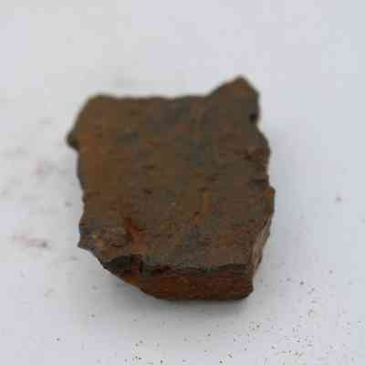 Closeup of basaltic glass core: A piece of basaltic glass core rests on a plain surface, displaying its rough texture alongside scattered grains and particles.