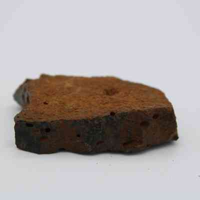 Basaltic glass core profile: The image shows a piece of basaltic glass with a rough texture, featuring a dark, weathered outer layer and small pits scattered across its surface.