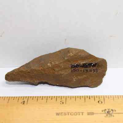 Small basalt awl (kui houhou) with item number: The image shows a pointed brown stone object placed on a white background, with a wooden ruler measuring it below.