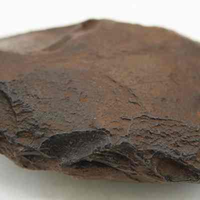 Closeup profile of a basalt adze blank: The image shows a weathered, brownish-gray stone tool with sharp edges, showcasing flaked surfaces.
