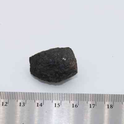 Closeup of basaltic glass core with ruler: The image shows a small, dark basaltic glass core placed beside a ruler for scale on a white surface.
