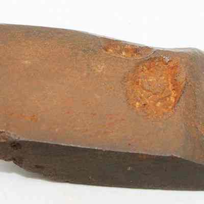 Basalt adze fragment: The image shows a close-up of a rugged, brown adze fragment with rough, uneven edges and a distinctly worn surface, indicating historical use.