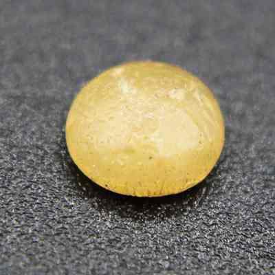 Closeup of plastic disk: A small, rough, yellow plastic disk with an opaque appearance sits on a textured gray surface.
