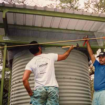 Two men installing mesh along top of water storage structure