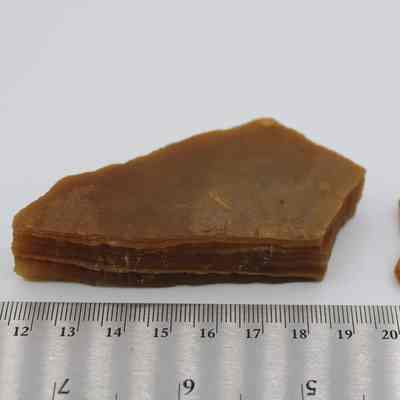 Two agate flakes with ruler: Two brown agate flakes are positioned on a white surface beside a silver ruler, with the larger flake displaying visible layered structures.