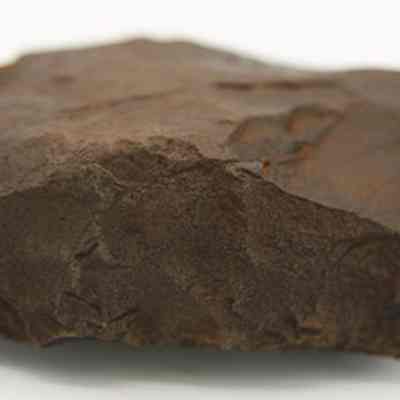 Closeup profile of a basalt adze blank: The image shows a rough, dark brown rock with angular surfaces, displayed against a plain, light background.