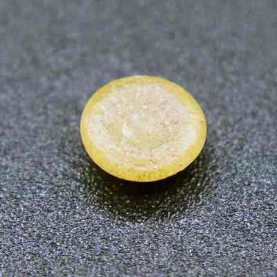 Closeup of plastic disk underside: The image shows a small, round, yellow object with a slightly rough texture, placed against a dark, textured background surface.