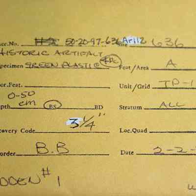 Artifact envelope for green plastic pieces: The image shows a detailed artifact label featuring various handwritten entries, including an accession number, artifact name, location details, and date.