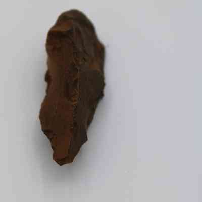 Lengthwise view of a possible auger: The image shows a brown, irregularly shaped object that resembles a piece of stone or rock, possibly an archaeological artifact or ancient tool.