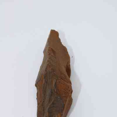 Lengthwise view of a possible auger: The image shows a pointed, rust-colored stone tool resembling an auger against a stark white background.