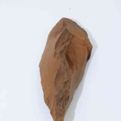 Lengthwise view of a possible auger: The image shows a roughly hewn, pointed stone tool, potentially resembling an ancient hand-crafted auger, set against a neutral white background.