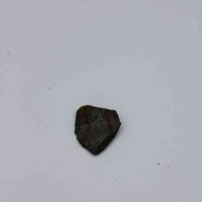 Closeup of tiny basaltic glass flake: The image shows a small, dark flake of basaltic glass lying on a plain, light-colored surface.